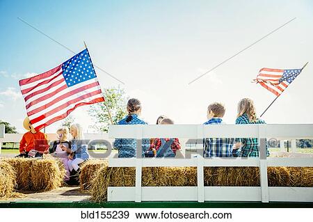 Stock Photo - Caucasian children waving American flags on hay ride. Fotosearch
