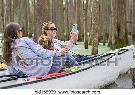 Stock Photo - Caucasian family taking cell phone photographs in canoes on river. Fotosearch