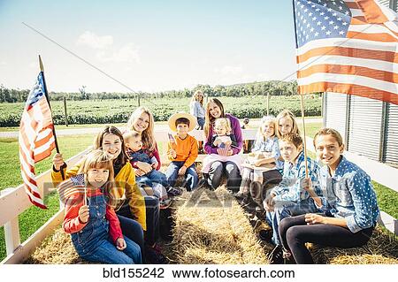 Stock Image - Caucasian family waving American flags on hay ride. Fotosearch