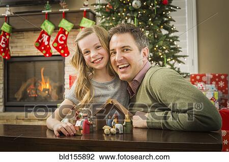 Stock Image - Caucasian father and daughter arranging nativity at Christmas. Fotosearch