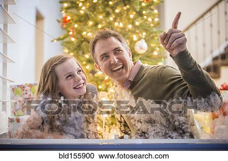 Stock Image - Caucasian father and daughter peering out frosty window at Christmas. Fotosearch