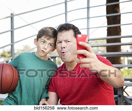 Stock Photo - Caucasian father and son taking cell phone photograph on bleachers. Fotosearch