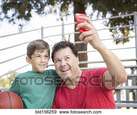 Stock Photo - Caucasian father and son taking cell phone photograph on bleachers. Fotosearch