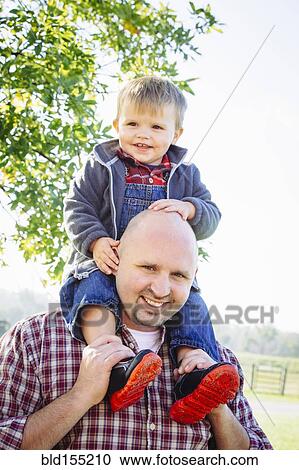 Stock Image - Caucasian father carrying son on shoulders. Fotosearch