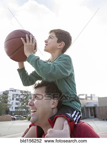 Stock Image - Caucasian father carrying son with basketball on shoulders. Fotosearch