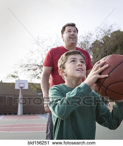 Stock Image - Caucasian father watching son hold basketball on court. Fotosearch