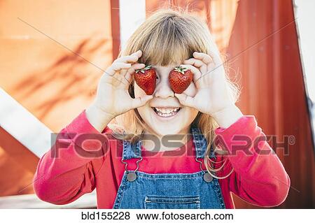 Stock Photo - Caucasian girl holding strawberries over eyes. Fotosearch