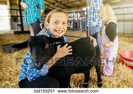 Stock Image - Caucasian girl petting goat in barn. Fotosearch