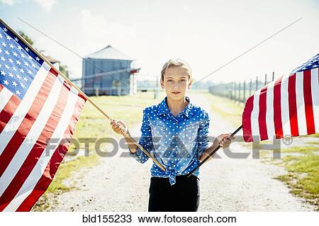 Stock Image - Caucasian girl waving American flags on farm. Fotosearch