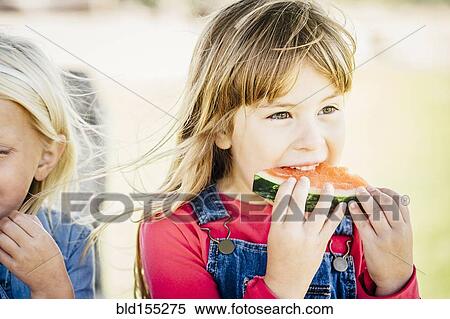Stock Photography - Caucasian girls eating watermelon outdoors. Fotosearch