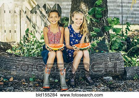 Picture - Caucasian girls eating watermelon under tree. Fotosearch