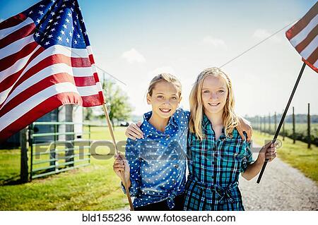 Stock Photograph - Caucasian girls waving American flags on farm. Fotosearch
