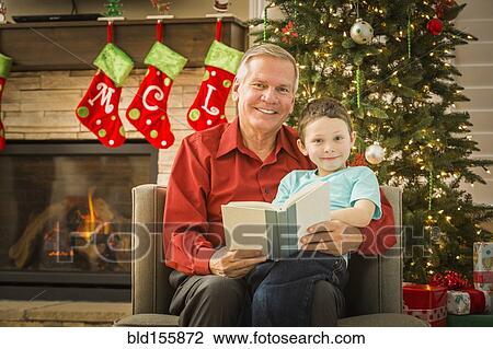 Stock Image - Caucasian grandfather reading to grandson at Christmas. Fotosearch