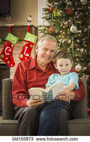 Stock Image - Caucasian grandfather reading to grandson at Christmas. Fotosearch