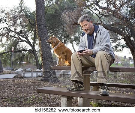 Stock Image - Caucasian man and dog sitting on picnic table in park. Fotosearch