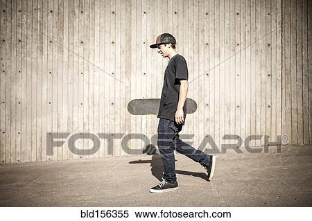 Stock Photography - Caucasian man carrying skateboard near wooden wall. Fotosearch