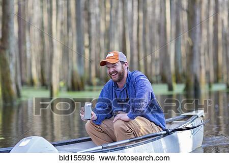 Stock Photograph - Caucasian man drinking beer in canoe on river. Fotosearch