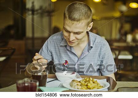Stock Photograph - Caucasian man eating lunch at table. Fotosearch
