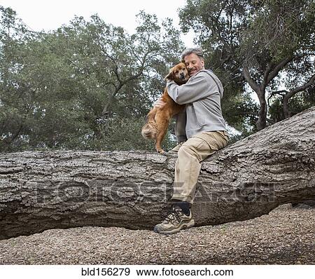 Stock Photo - Caucasian man hugging dog on tree in park. Fotosearch