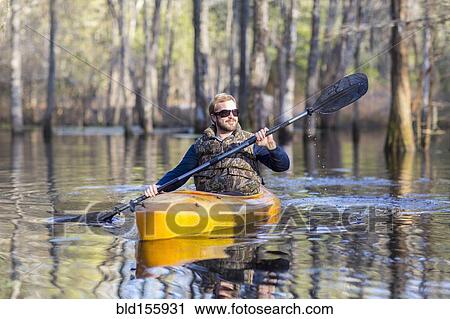 Stock Image - Caucasian man rowing canoe in river. Fotosearch