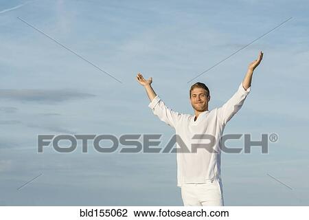 Stock Image - Caucasian man standing with arms raised outdoors. Fotosearch