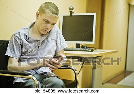 Stock Photography - Caucasian man using cell phone at computer desk. Fotosearch