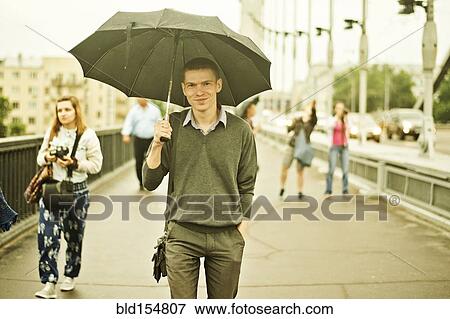 Stock Photo - Caucasian man walking under umbrella on sidewalk. Fotosearch