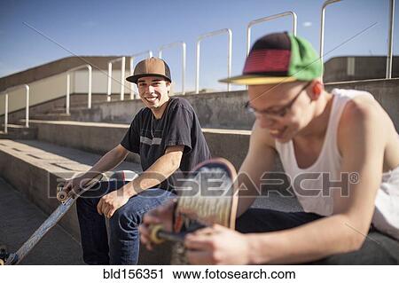 Stock Image - Caucasian men with skateboards sitting on steps. Fotosearch