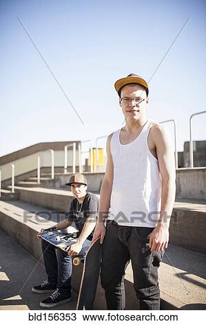 Stock Image - Caucasian men with skateboards sitting on steps. Fotosearch