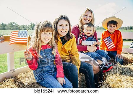 Stock Image - Caucasian mother and children waving American flags on hay ride. Fotosearch