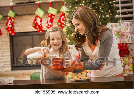 Stock Photography - Caucasian mother and daughter leaving cookies and milk for Santa at Christmas. Fotosearch