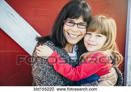 Stock Image - Caucasian mother and daughter smiling outside barn. Fotosearch