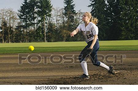 Stock Photo - Caucasian softball player pitching ball in field. Fotosearch