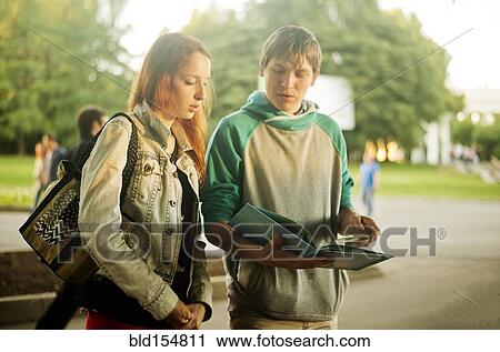 Stock Image - Caucasian students reading book in park. Fotosearch