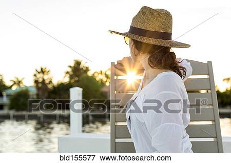 Stock Photo - Caucasian woman admiring sunset from deck chair. Fotosearch
