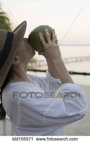 Stock Image - Caucasian woman drinking juice from coconut. Fotosearch