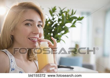Stock Image - Caucasian woman drinking juice in living room. Fotosearch