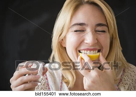 Stock Image - Caucasian woman eating lemon slice with liquor shot. Fotosearch