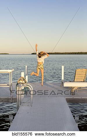 Stock Photograph - Caucasian woman jumping for joy on pier. Fotosearch