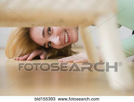 Stock Image - Caucasian woman peeking under chair. Fotosearch