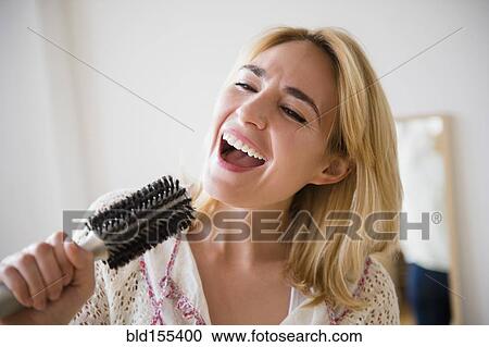 Stock Image - Caucasian woman singing into hairbrush. Fotosearch