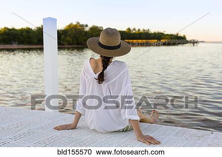 Stock Image - Caucasian woman sitting at edge of pier. Fotosearch