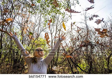 Stock Image - Caucasian woman throwing autumn leaves in forest. Fotosearch