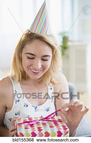 Stock Photo - Caucasian woman unwrapping birthday present at party. Fotosearch