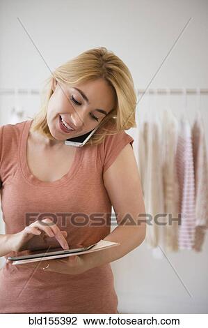 Stock Image - Caucasian woman using digital tablet in clothing store. Fotosearch