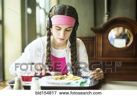 Stock Photo - Caucasian woman wearing headphones eating in dining room. Fotosearch