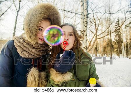 Stock Photography - Caucasian women blowing bubbles in snowy field. Fotosearch