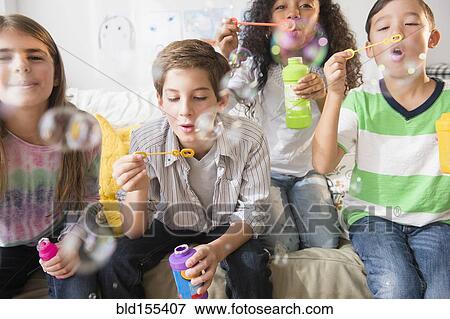 Stock Photo - Children blowing bubbles on sofa. Fotosearch