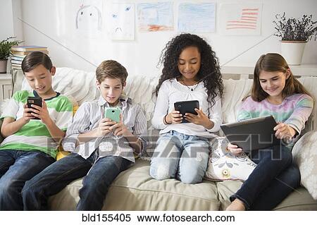 Stock Photography - Children using cell phones and digital tablets on sofa. Fotosearch