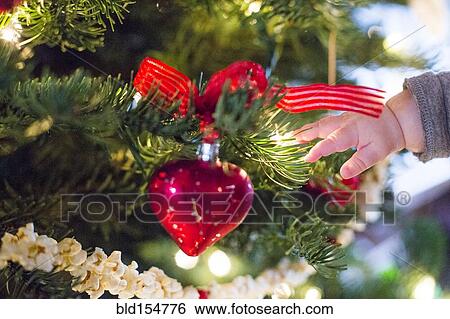 Stock Photograph - Close up of hand of Caucasian baby girl near Christmas tree. Fotosearch